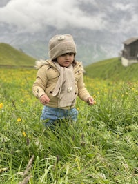 a little girl standing in a meadow with mountains in the background