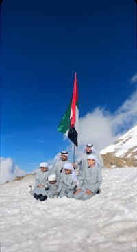 a group of people sitting on top of a snowy mountain with an uae flag