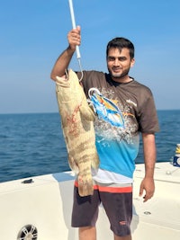 a man holding up a large fish on a boat