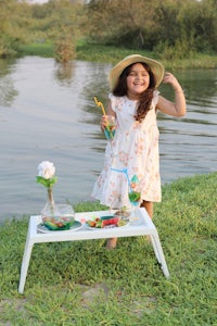 a girl in a hat standing next to a table in a grassy area