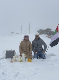 two men sitting in the snow with a flag