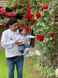 a man holding a baby in front of roses